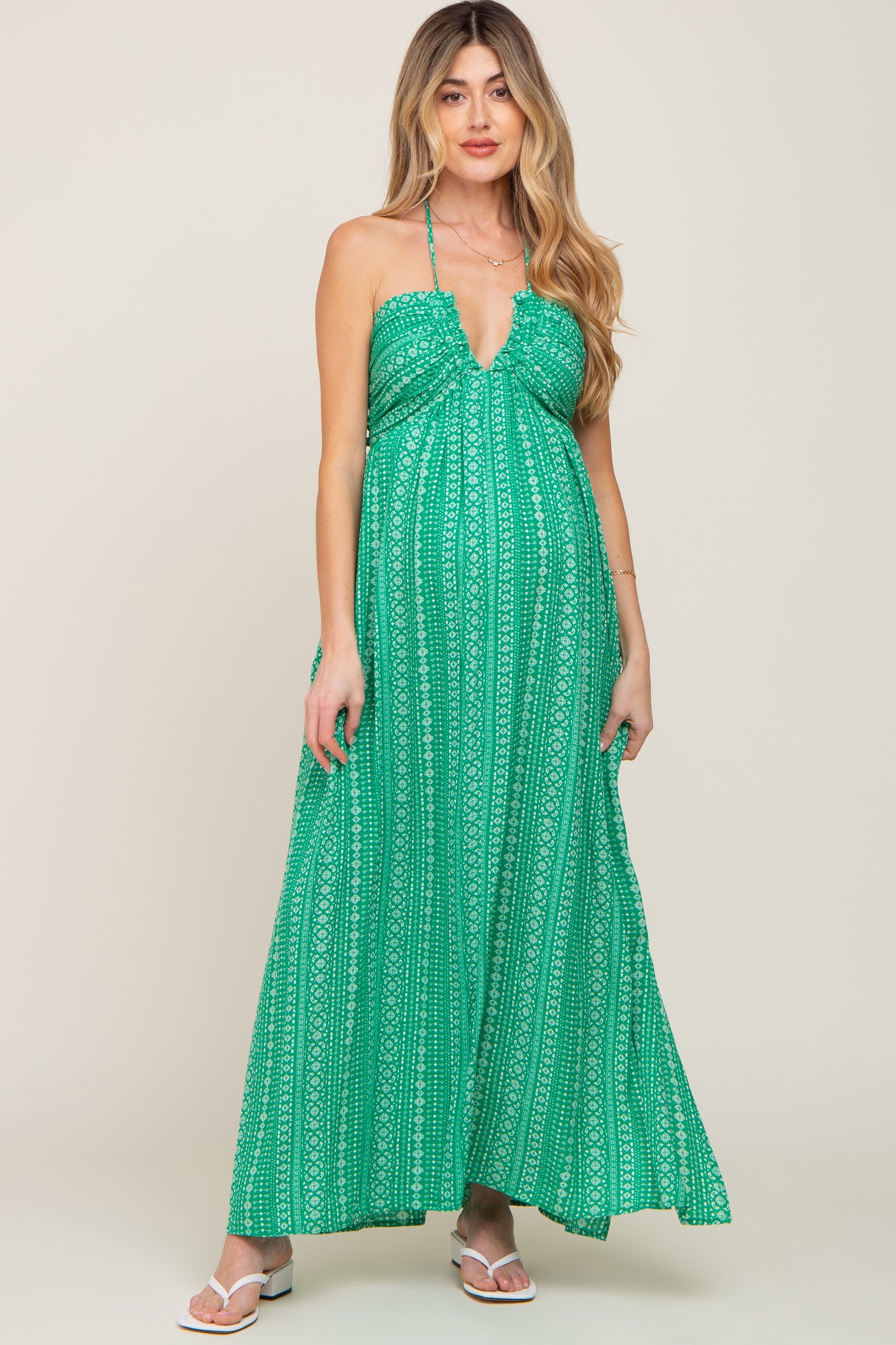 woman wearing a green printed halter neck maternity maxi dress with white sandals