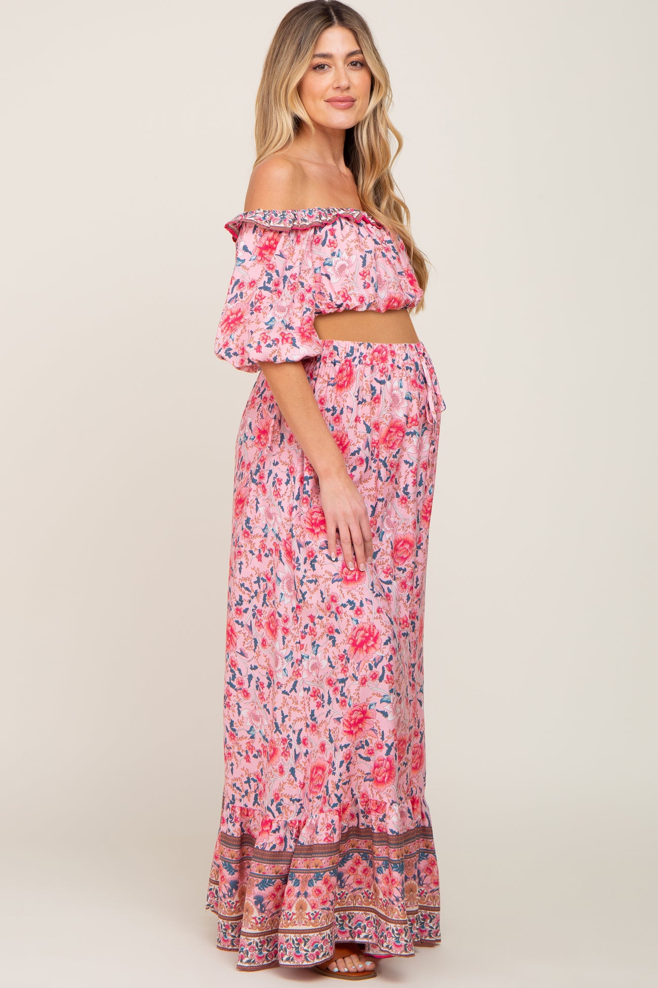 woman wearing a pink floral off-shoulder maternity crop top and matching maxi skirt, showing her baby bump