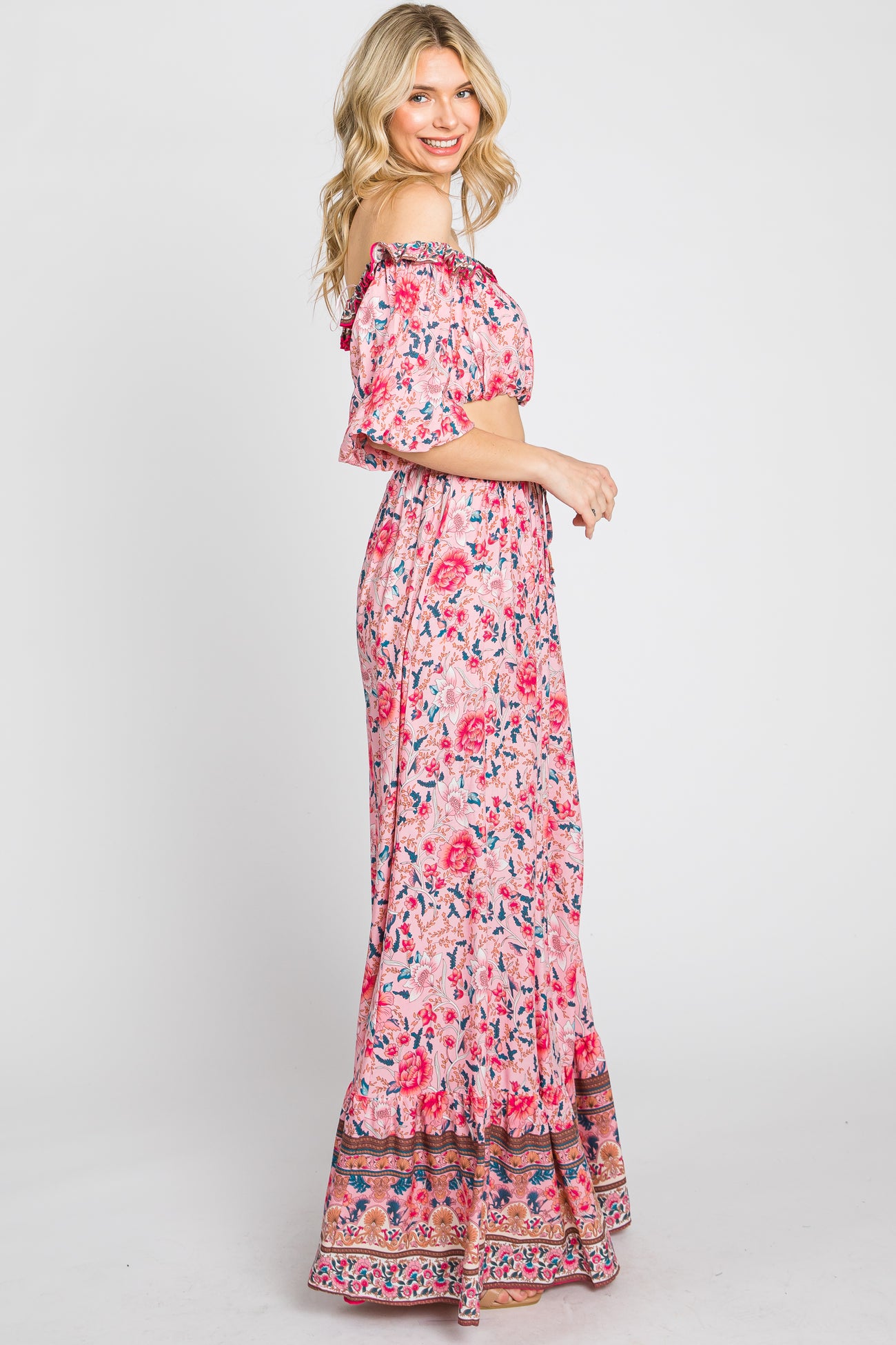 woman wearing a pink floral off-the-shoulder maxi dress with short sleeves and a patterned hem