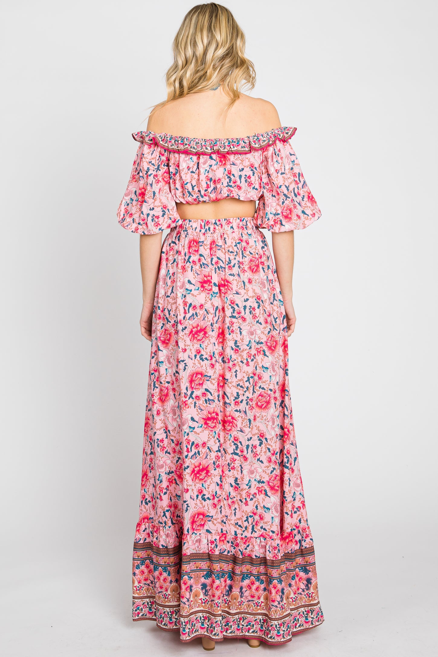 woman wearing a pink floral maxi dress with off-the-shoulder sleeves and a cropped back design