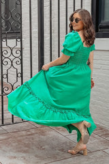 woman in green puff sleeve maxi dress and tan block heel sandals posing by a black wrought iron gate