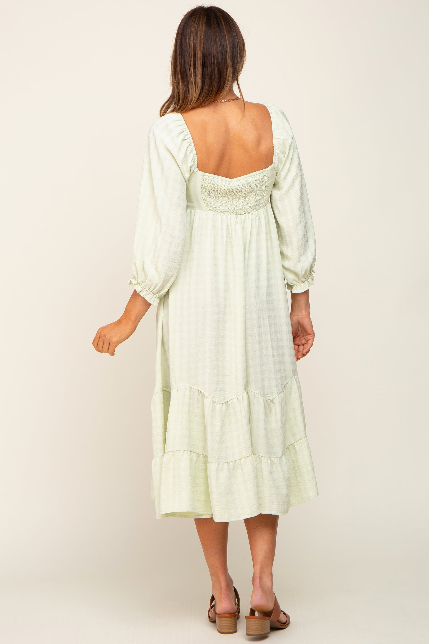 back view of woman wearing light green smocked midi dress with long puff sleeves and tiered skirt