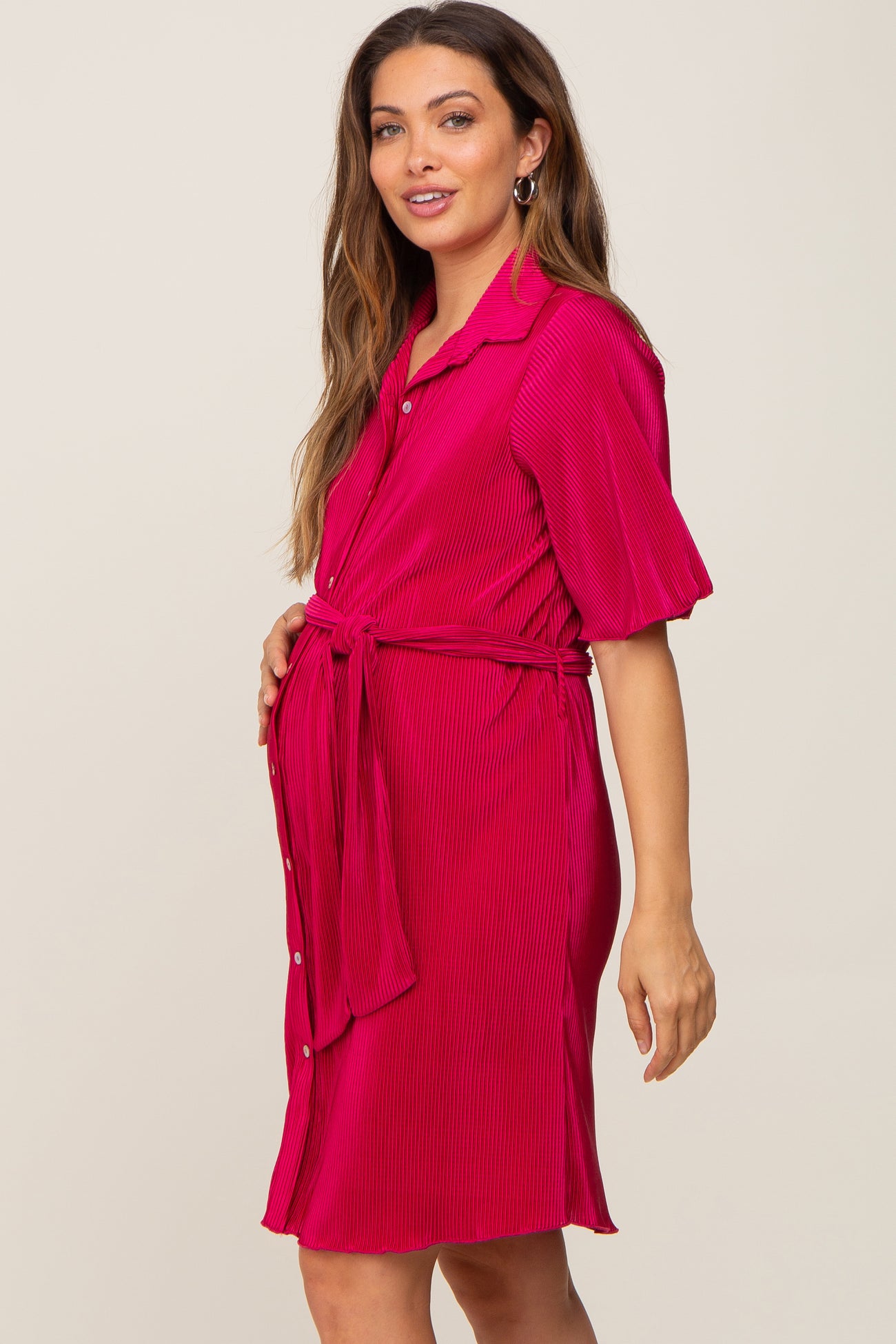 woman wearing a bright pink short sleeve maternity dress with a tie waist and visible baby bump