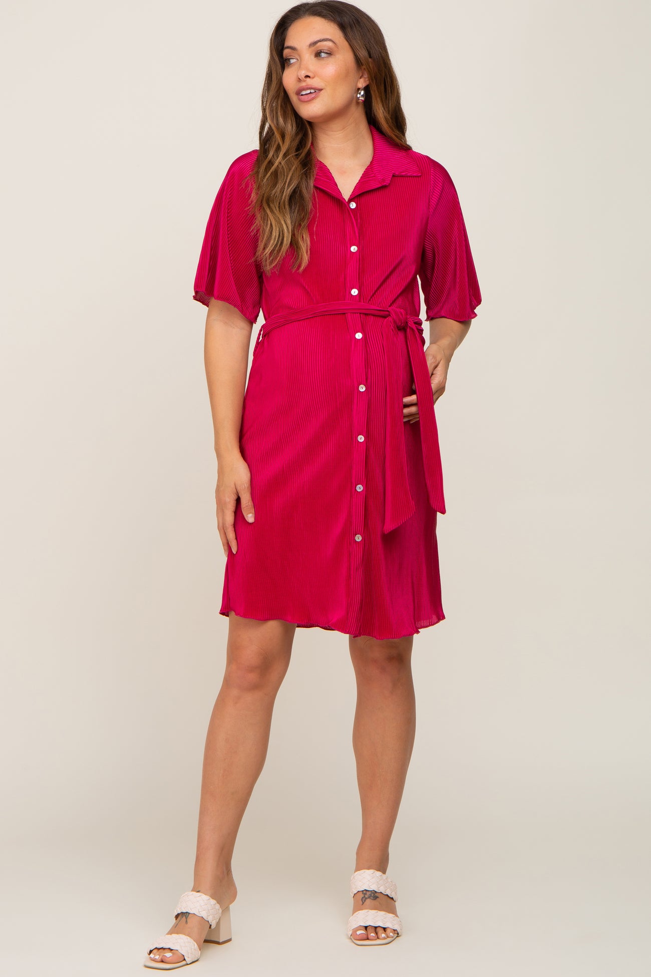 woman wearing a bright pink button-down maternity dress with short sleeves and a belted waist