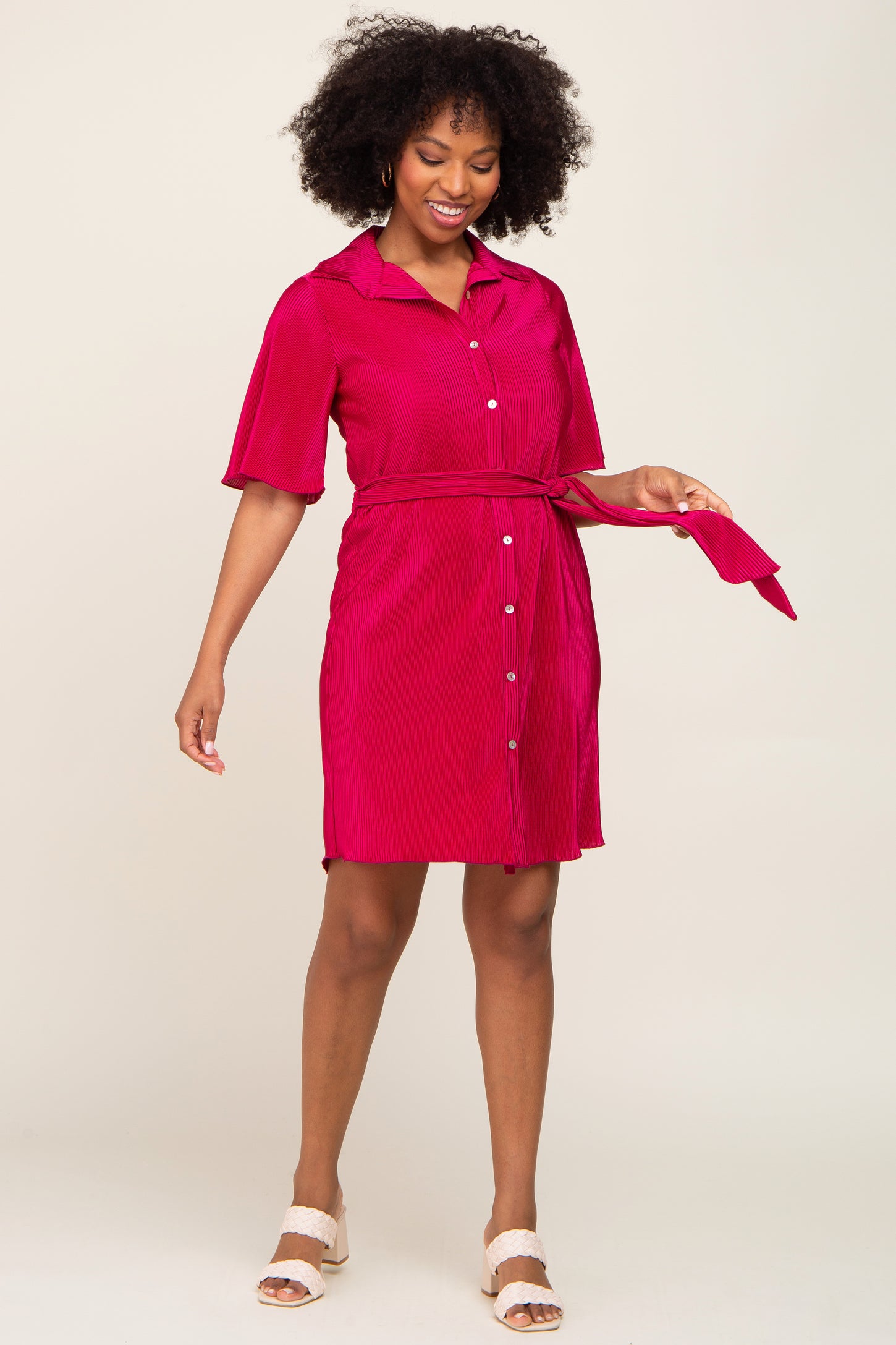 woman wearing a bright pink short sleeve button-up belted dress with a collar and tie detail