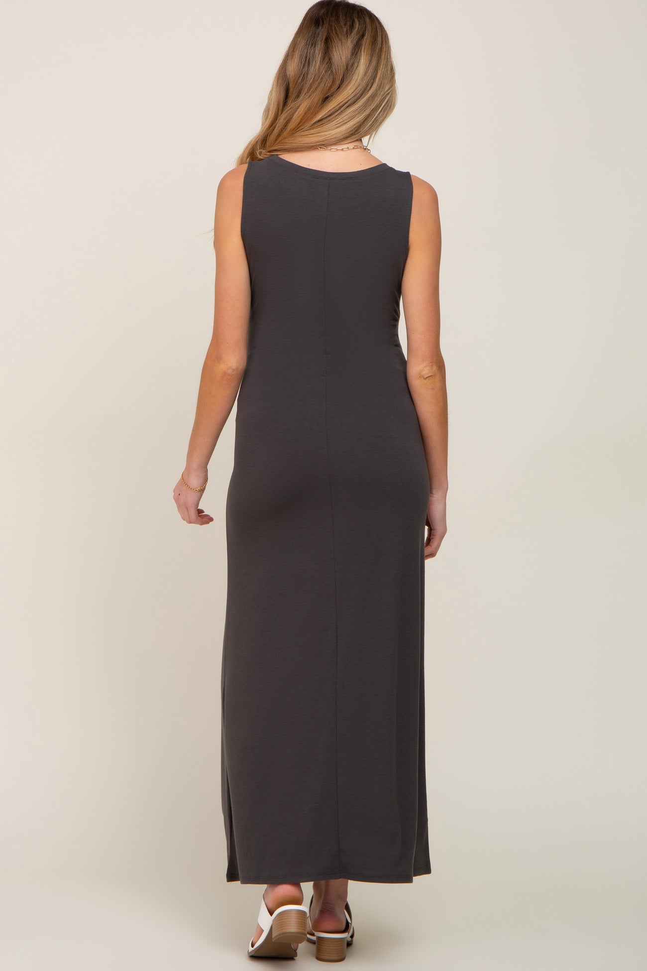 Back view of a woman wearing a charcoal grey sleeveless maxi dress and white block heel sandals