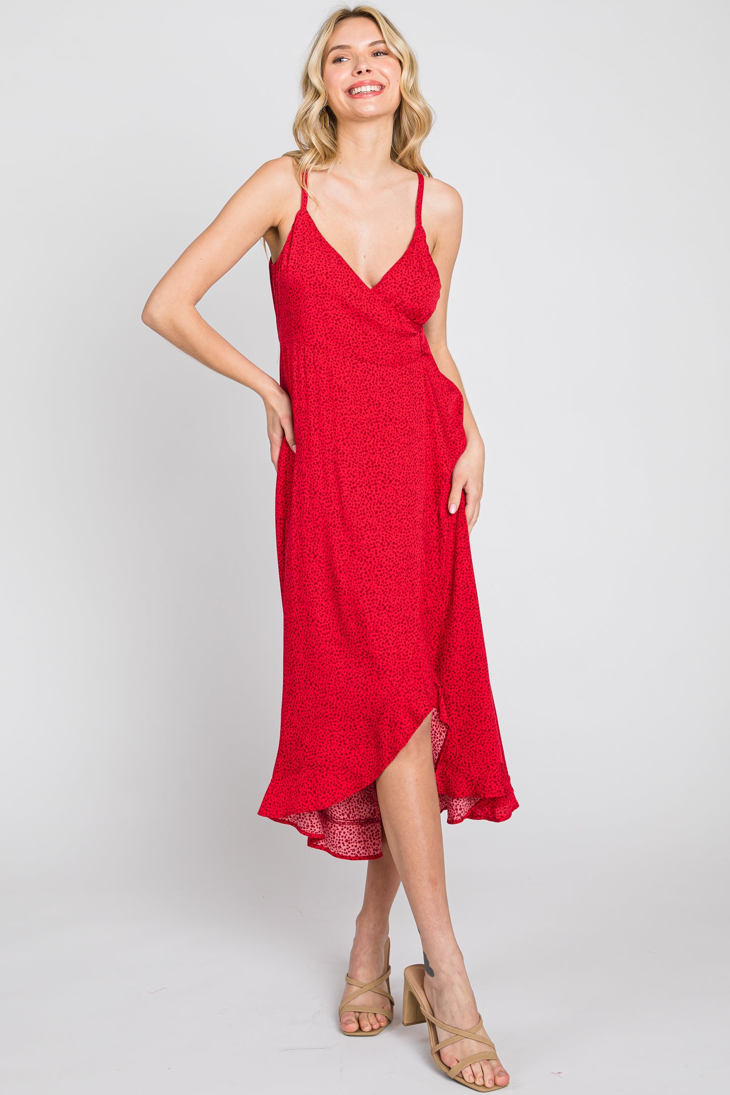 woman wearing a red sleeveless midi dress with a v-neck and high-low hemline, smiling against a plain background