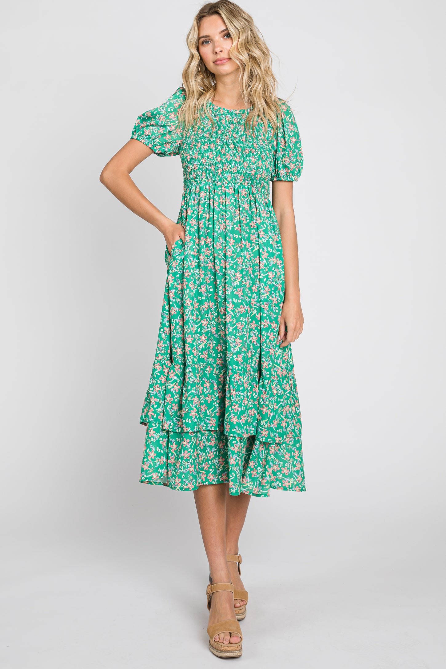 Woman wearing a green floral smocked midi dress with puff sleeves and tiered skirt