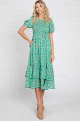 Woman wearing a green floral smocked midi dress with puff sleeves and tiered skirt