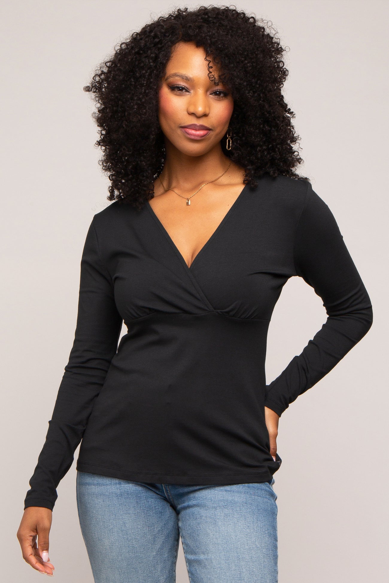 Woman with curly hair wearing a black long-sleeve v-neck wrap top and blue jeans