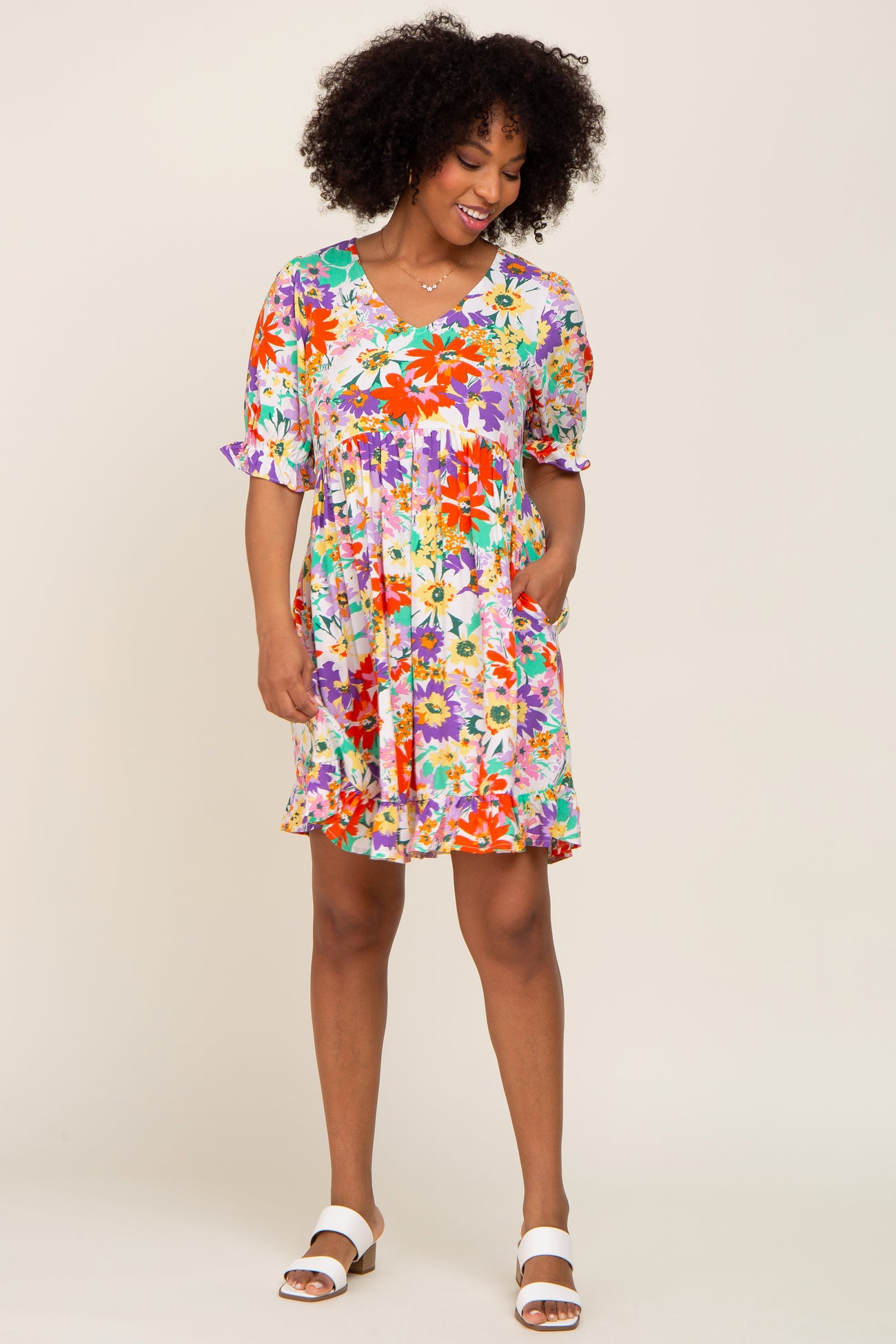 woman with afro hair wearing a colorful floral print babydoll dress and white sandals