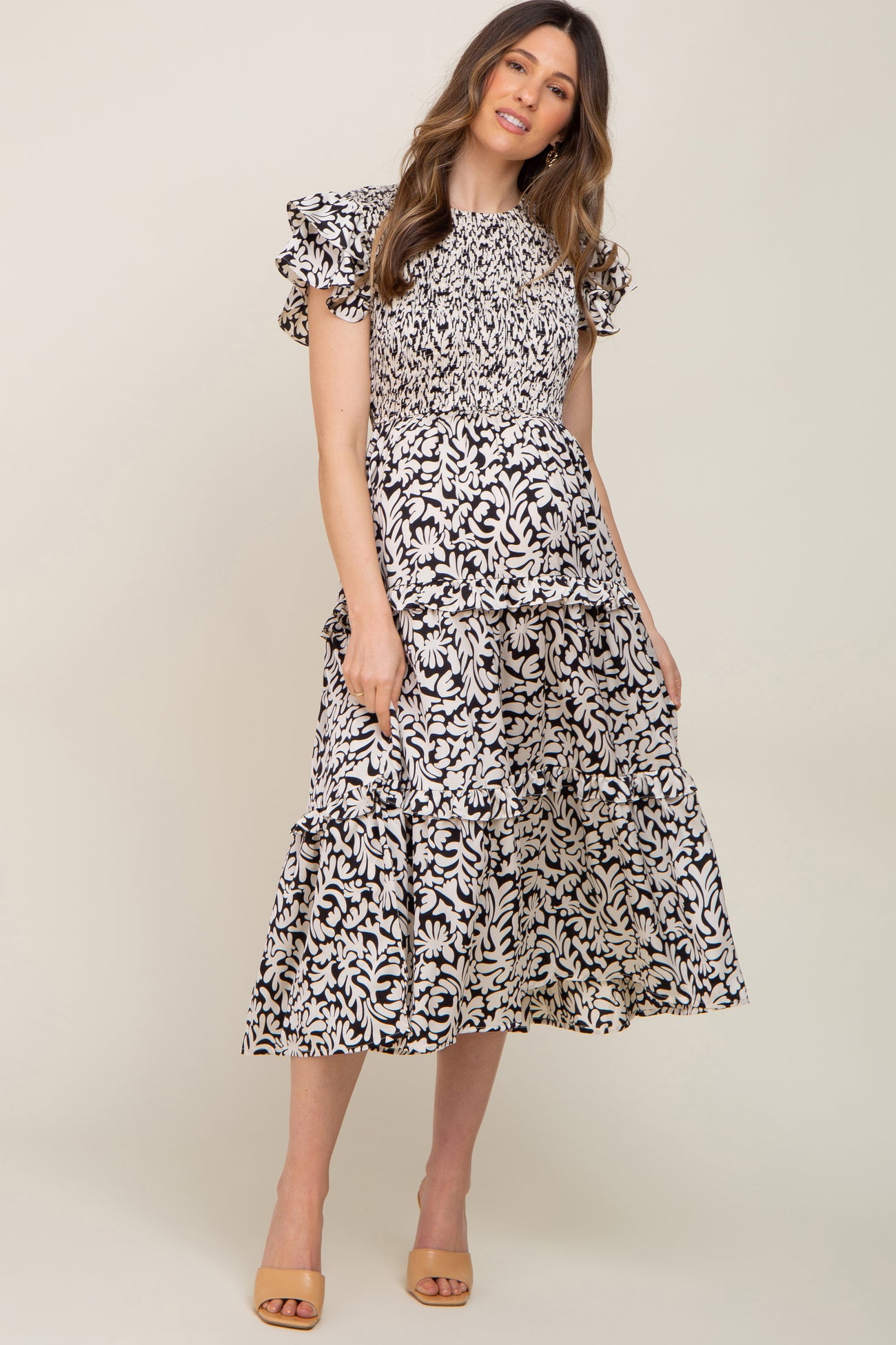 woman wearing a black and white floral print smocked maternity midi dress with ruffle sleeves