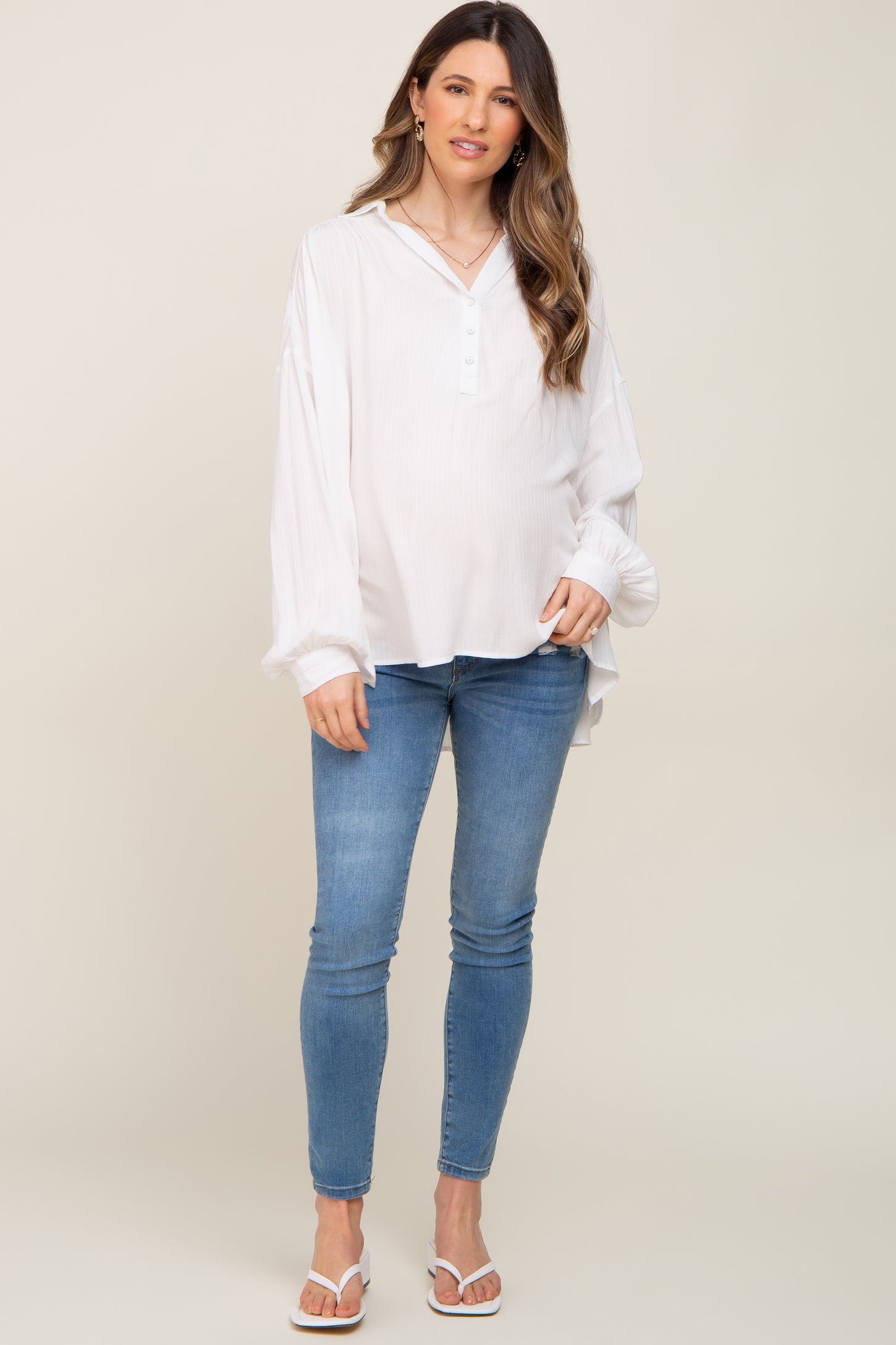 pregnant woman wearing white long sleeve maternity blouse and blue skinny jeans