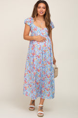 Pregnant woman in a light blue floral maternity midi dress with puff sleeves holding a straw bag