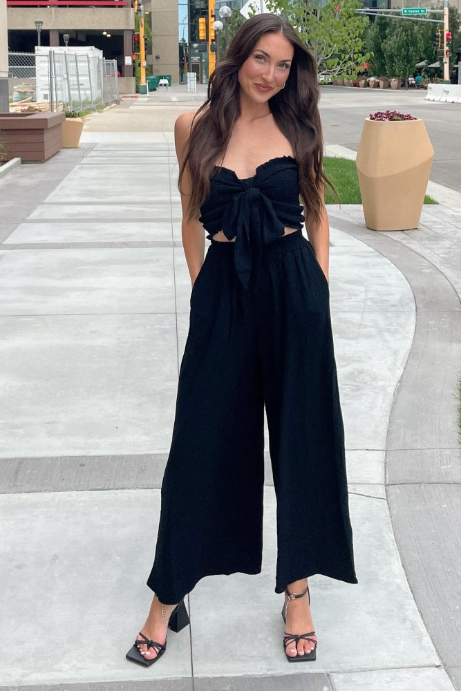 woman wearing a black strapless tie-front crop top and matching wide-leg pants on a city sidewalk