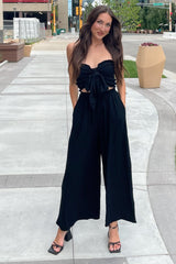 woman wearing a black strapless tie-front crop top and matching wide-leg pants on a city sidewalk