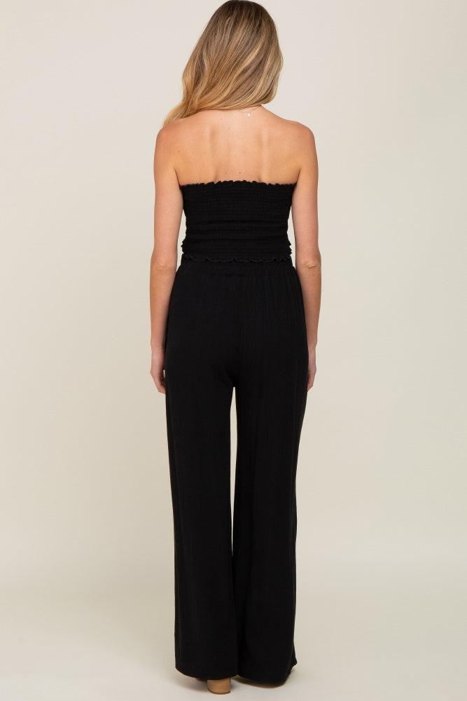 Back view of a woman wearing a black strapless jumpsuit with a smocked bodice and wide-leg pants