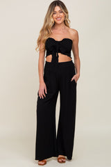 woman wearing a black strapless tie-front crop top and matching wide-leg pants set