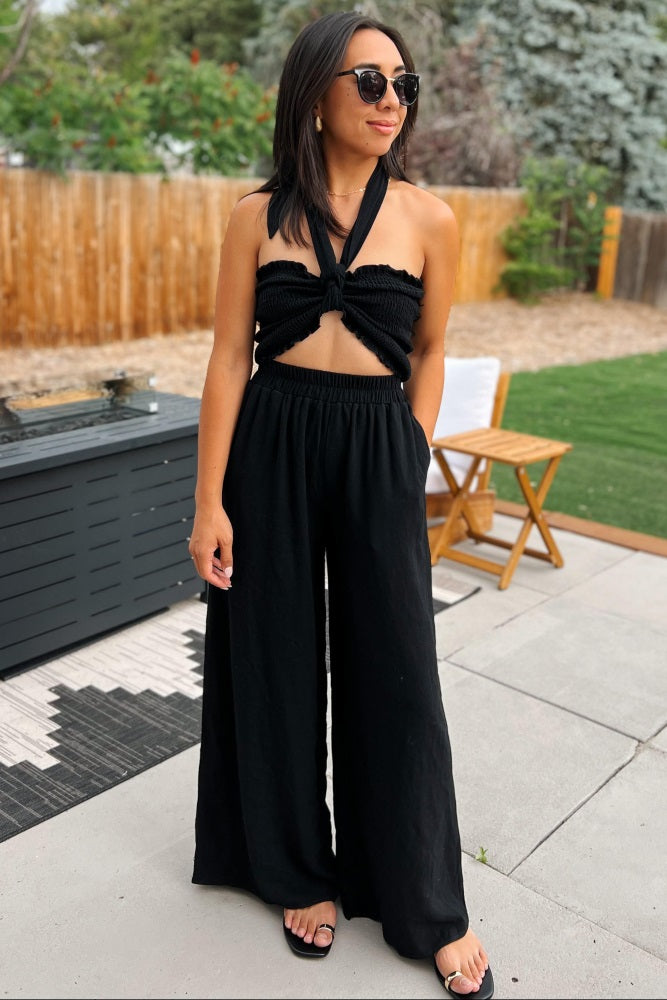 woman wearing black smocked halter top and wide leg pants with sunglasses standing on a patio