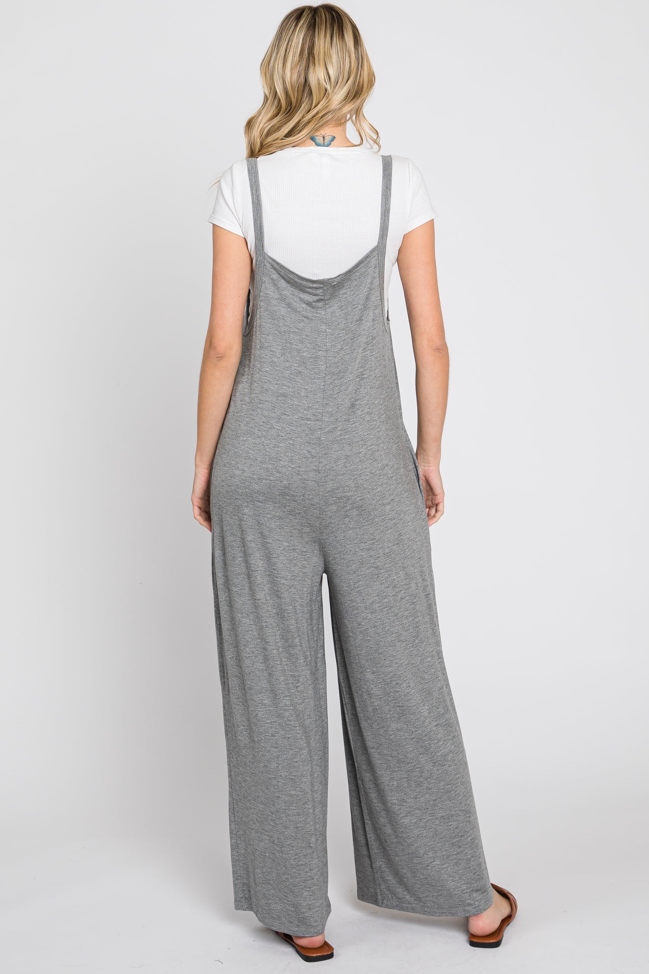 woman wearing a gray sleeveless jumpsuit with wide legs, viewed from the back