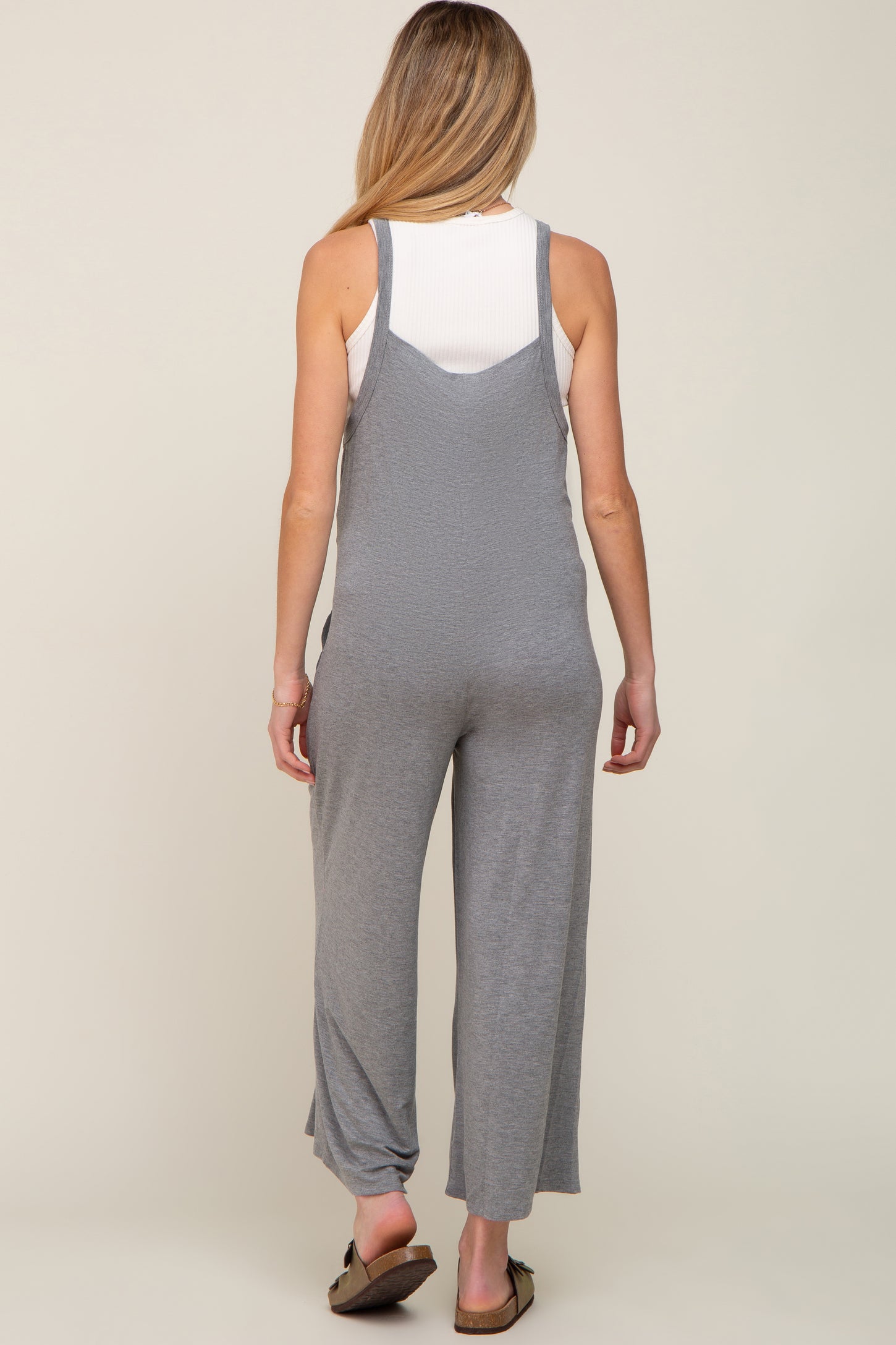 Back view of a woman wearing a grey maternity jumpsuit over a white ribbed tank top
