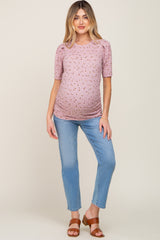 woman wearing a pink floral print maternity top with short puff sleeves and a visible baby bump, paired with blue jeans
