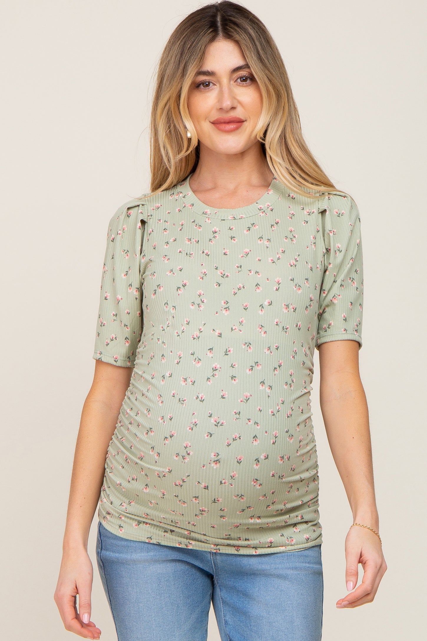 woman wearing a green short sleeve maternity top with floral print and ruched sides, showing her baby bump