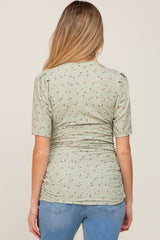 back view of a woman wearing a light green floral maternity top with short sleeves and ruching details