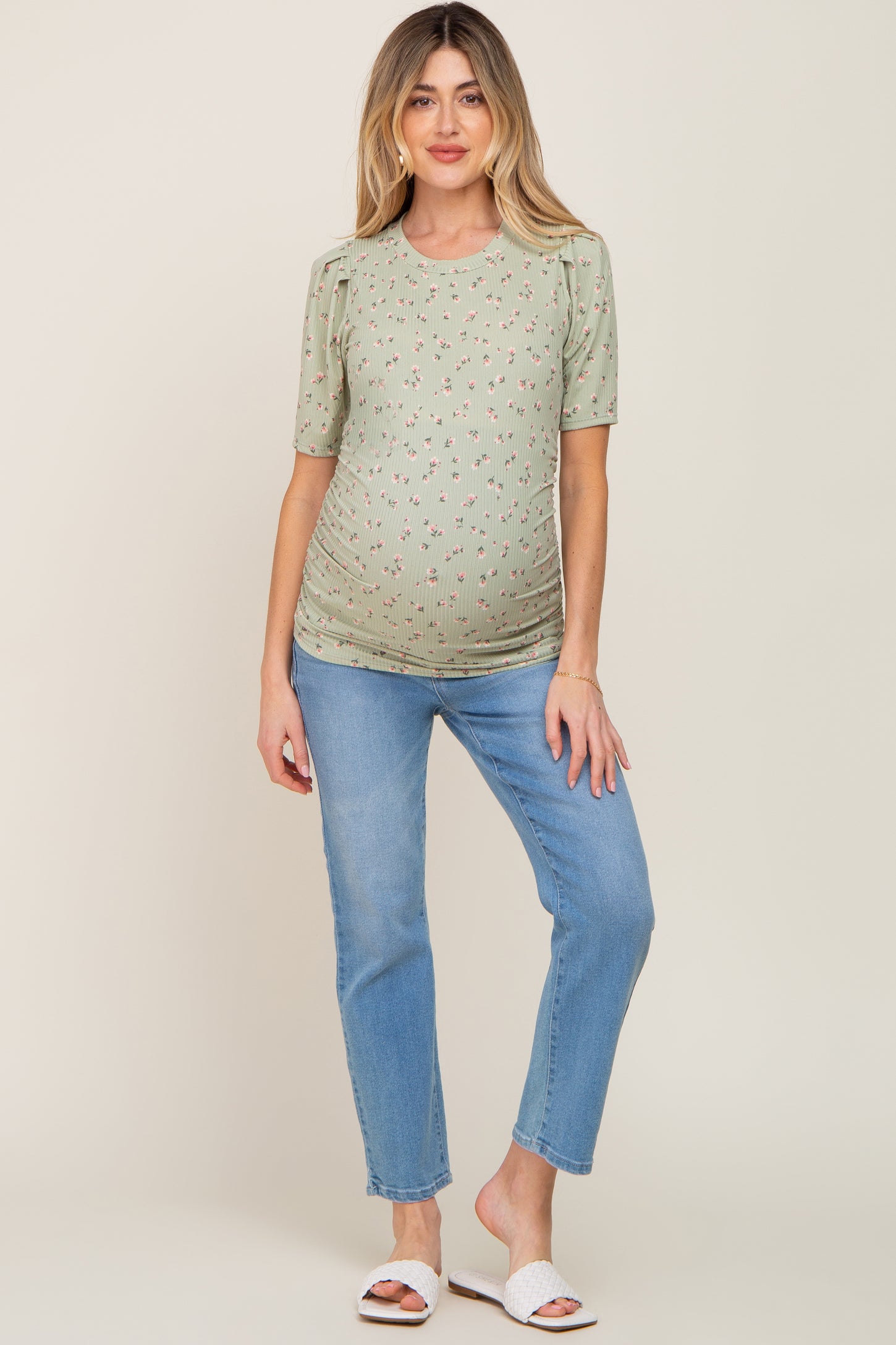 woman wearing a green short sleeve maternity top with floral print and paired with light blue jeans, showing her baby bump