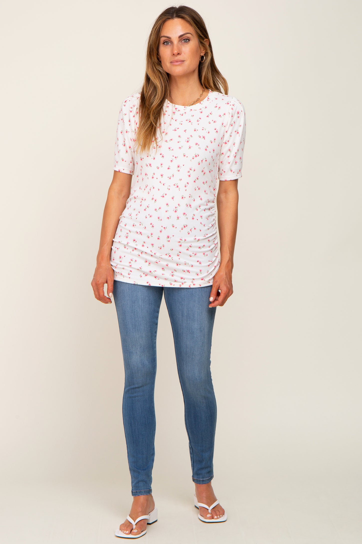 woman wearing a white short sleeve top with floral print and ruched sides paired with blue skinny jeans