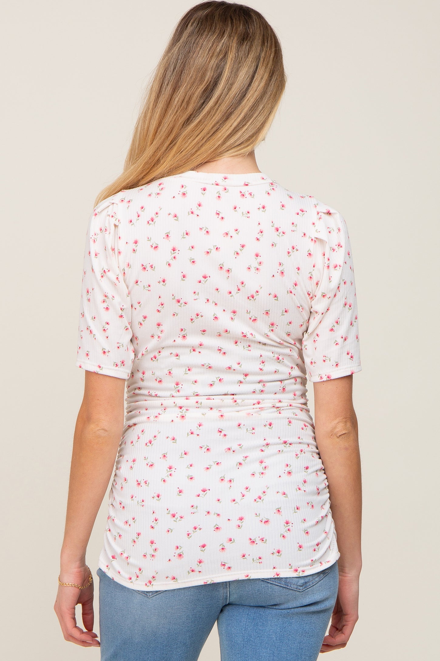 woman wearing a cream short sleeve maternity top with pink floral print and gathered sides