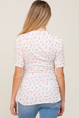 woman wearing a cream short sleeve maternity top with pink floral print and gathered sides