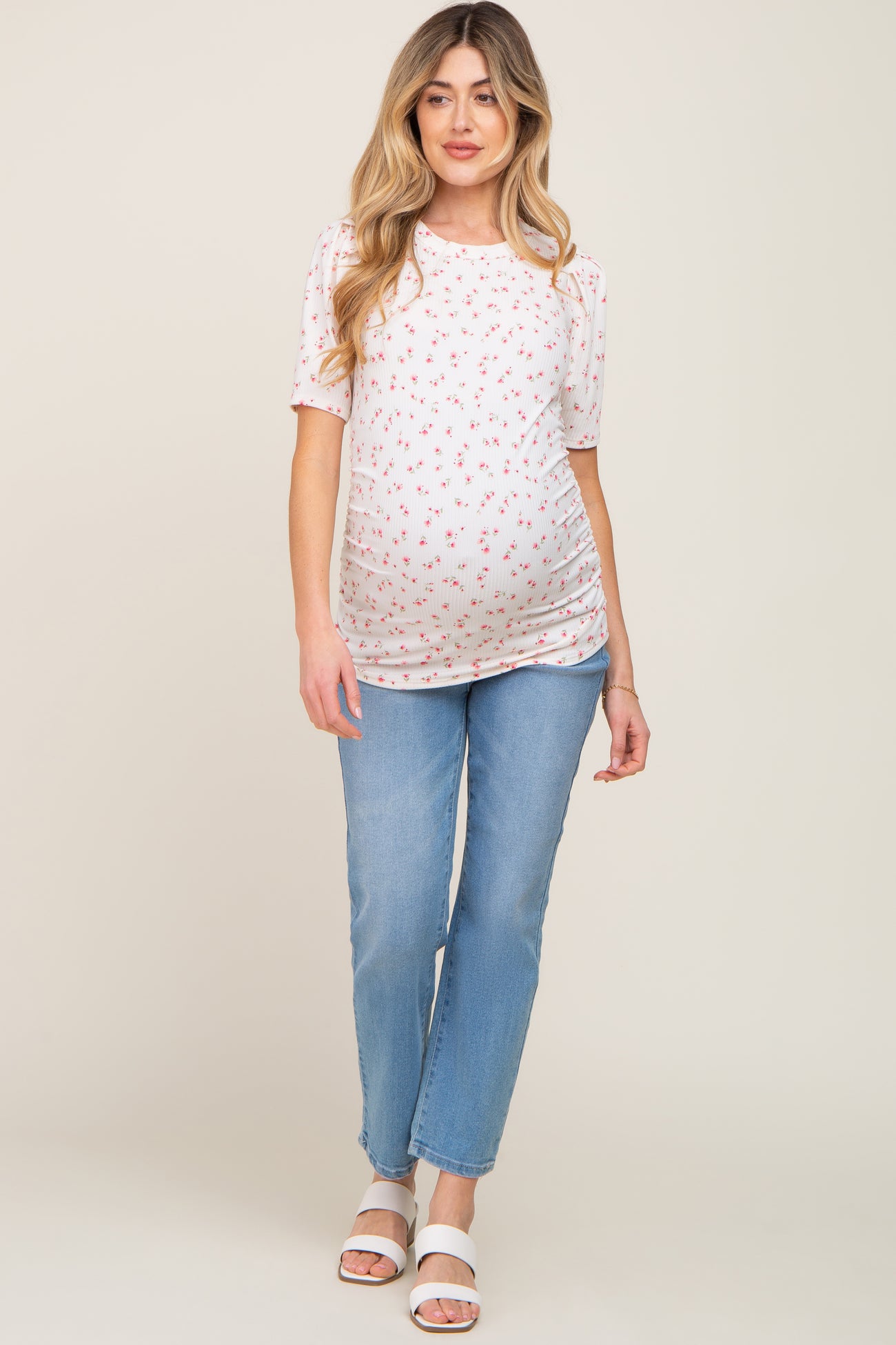 woman wearing a short sleeve floral maternity top and light blue jeans, showing her baby bump