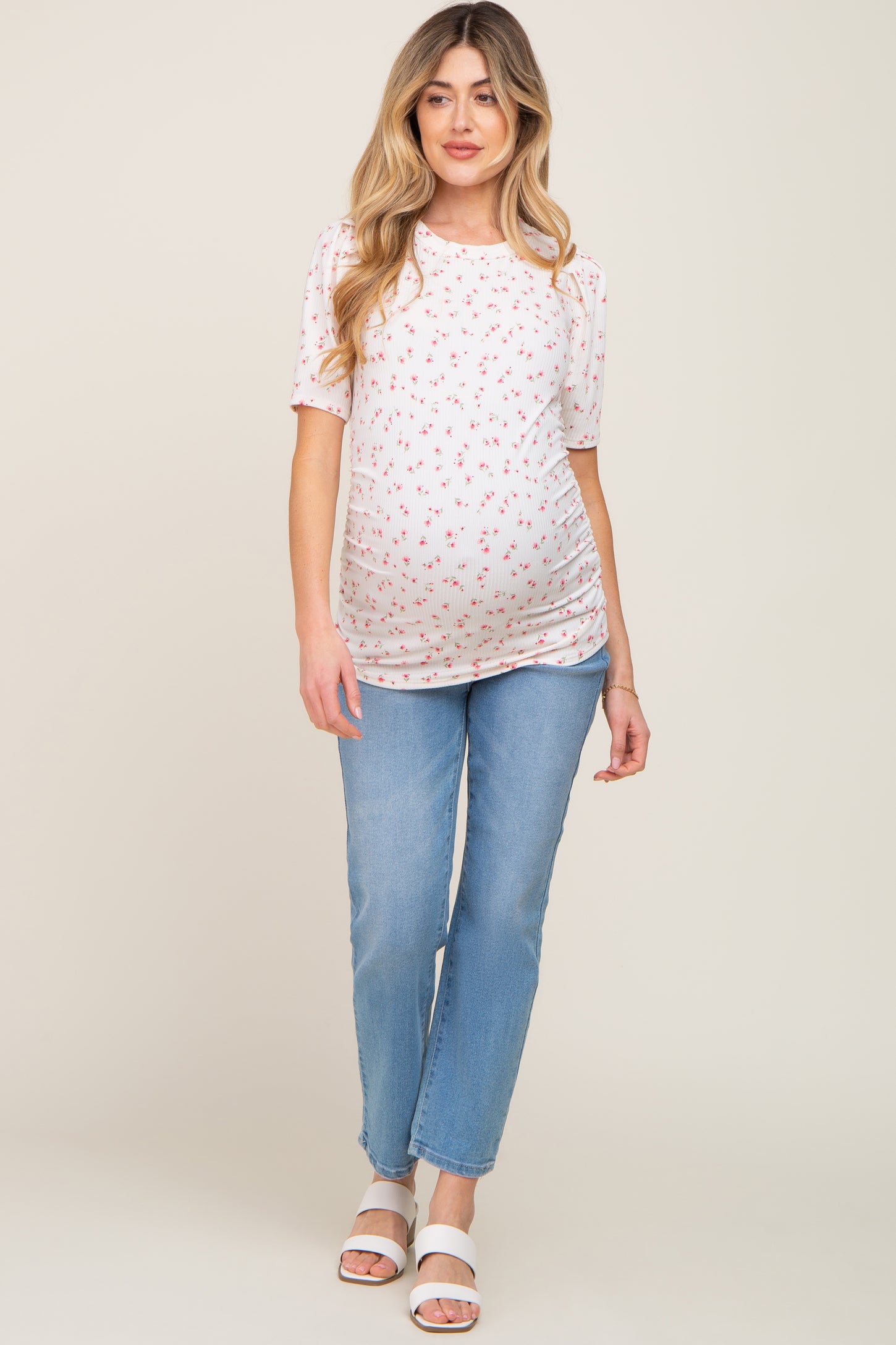woman wearing a short sleeve floral maternity top and light blue jeans, showing her baby bump