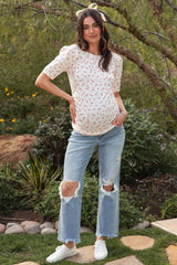 woman wearing a white short sleeve maternity top with red floral print and holding her baby bump, paired with ripped denim jeans