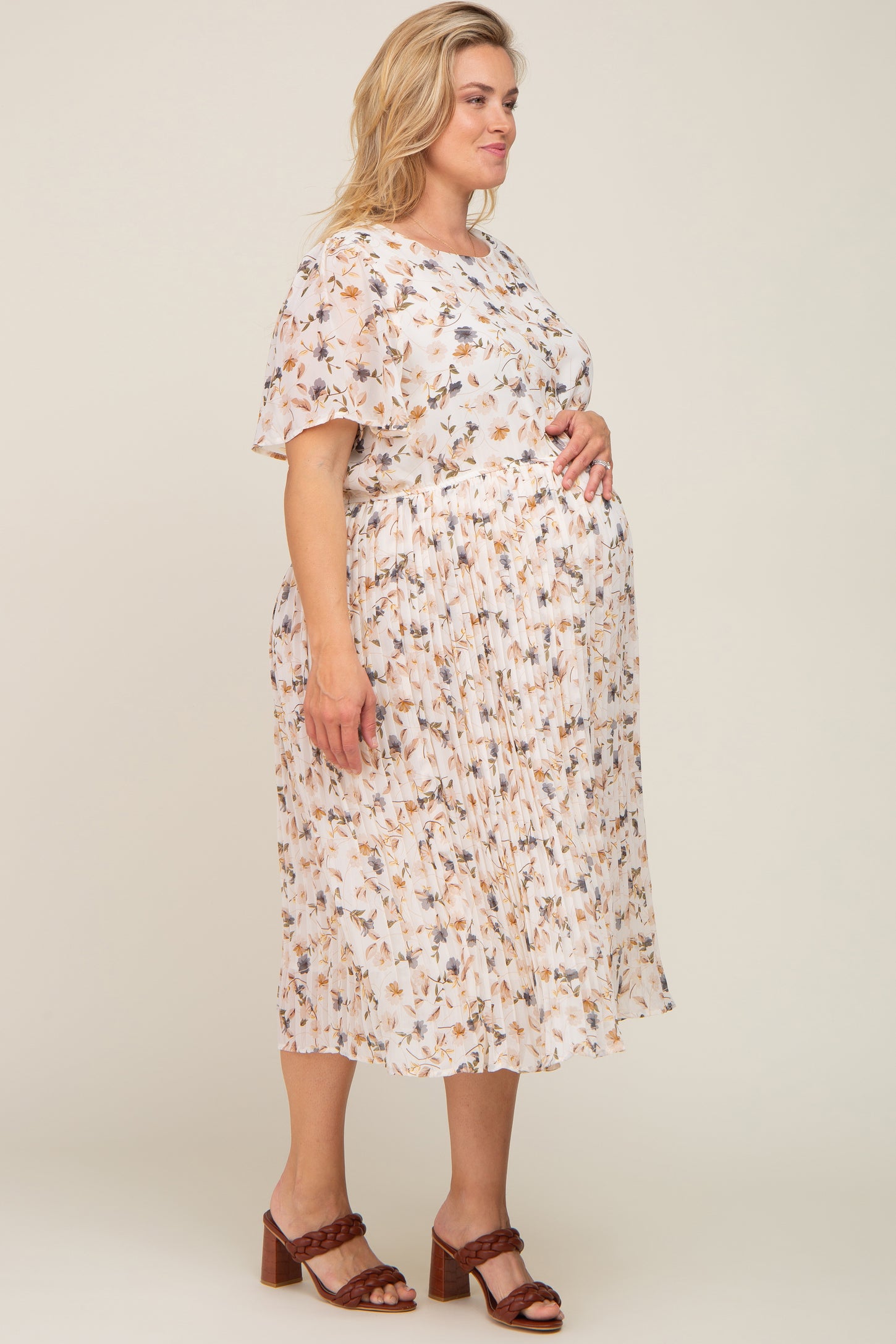 Pregnant woman wearing a floral pleated maternity midi dress and brown braided heels