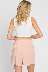 Back view of a woman wearing a white ribbed crop tank top and peach high-waisted paperbag shorts