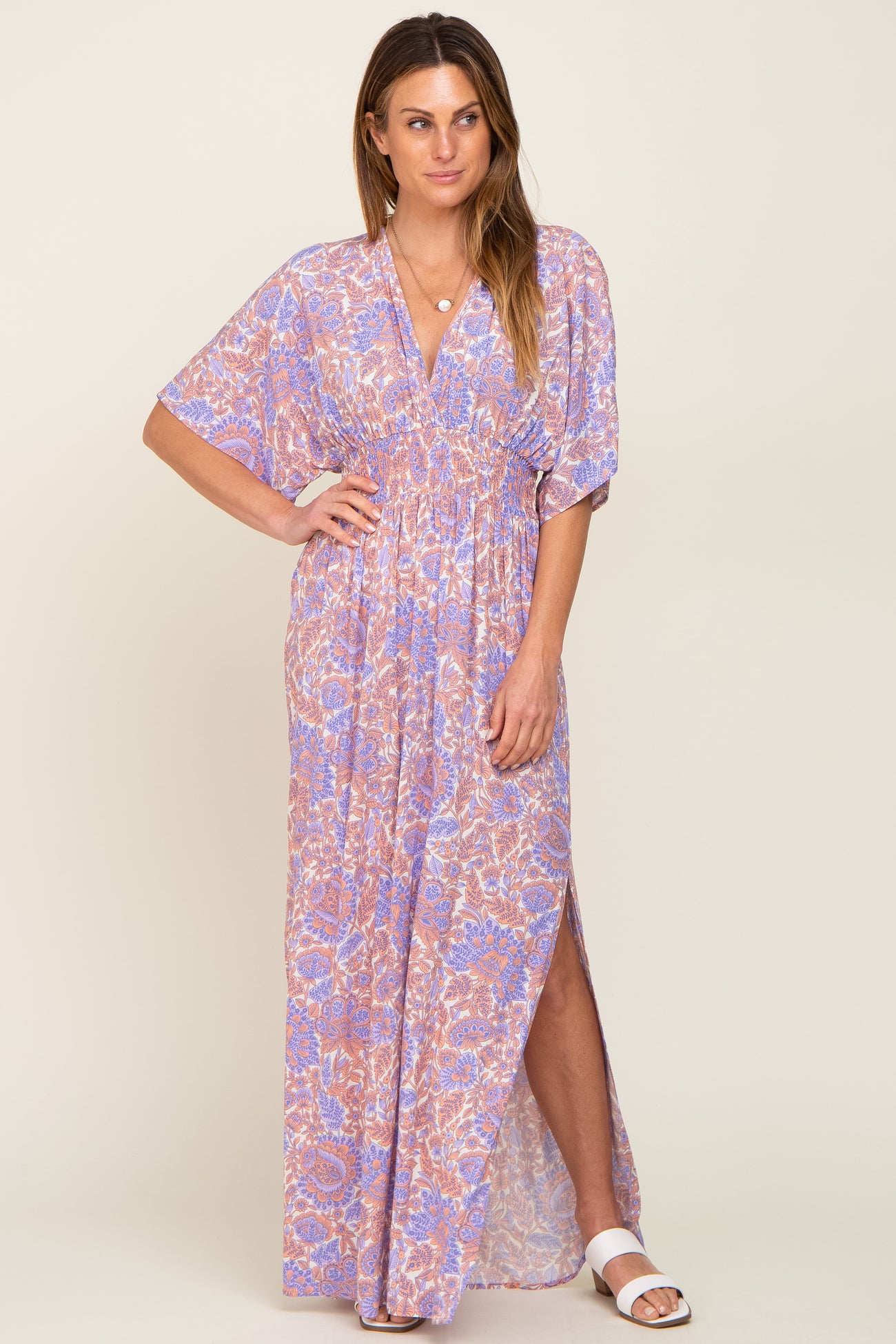 woman wearing a purple and orange floral print maxi dress with a smocked waist and side slit