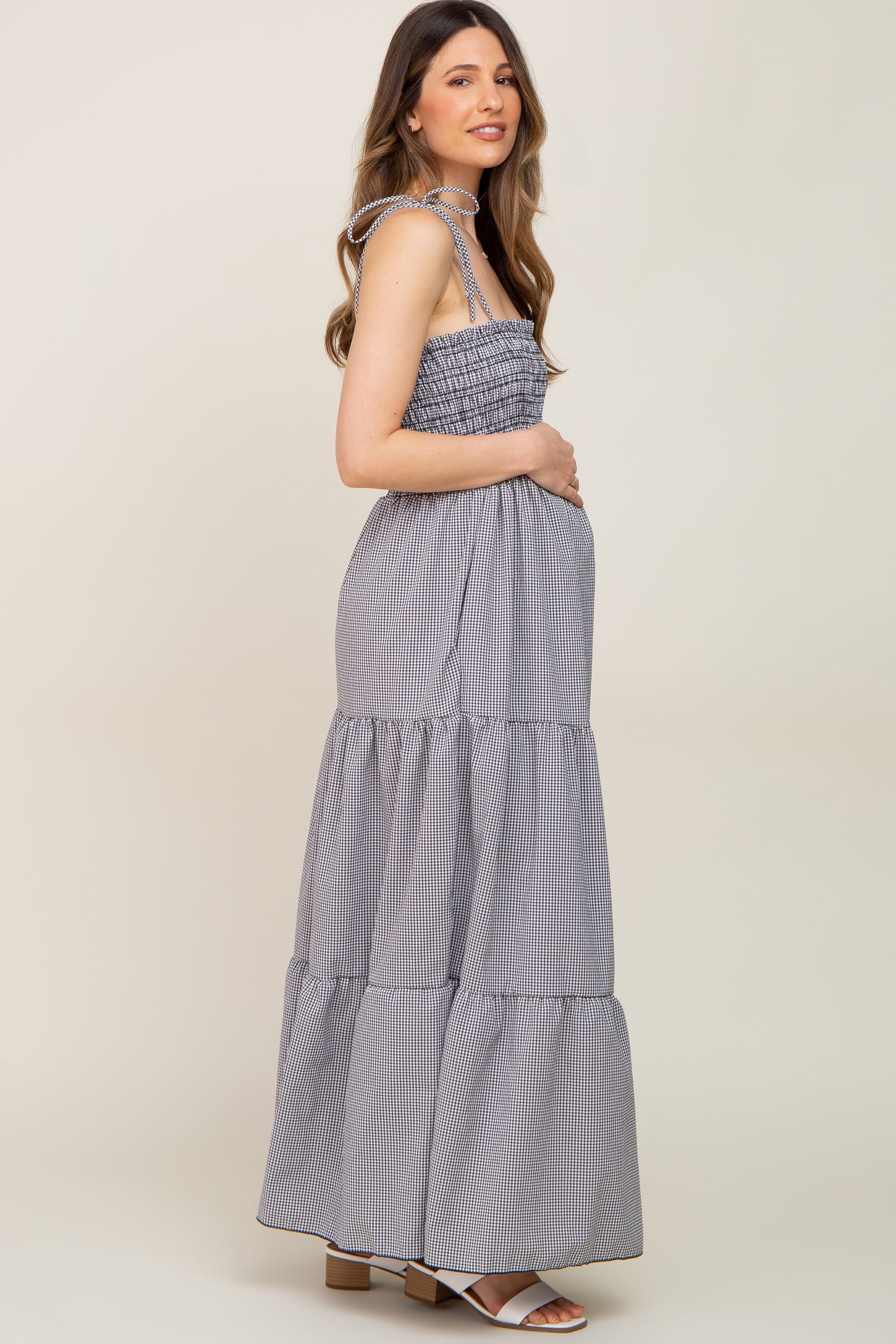 Pregnant woman in a black and white gingham tiered maternity maxi dress with tie straps