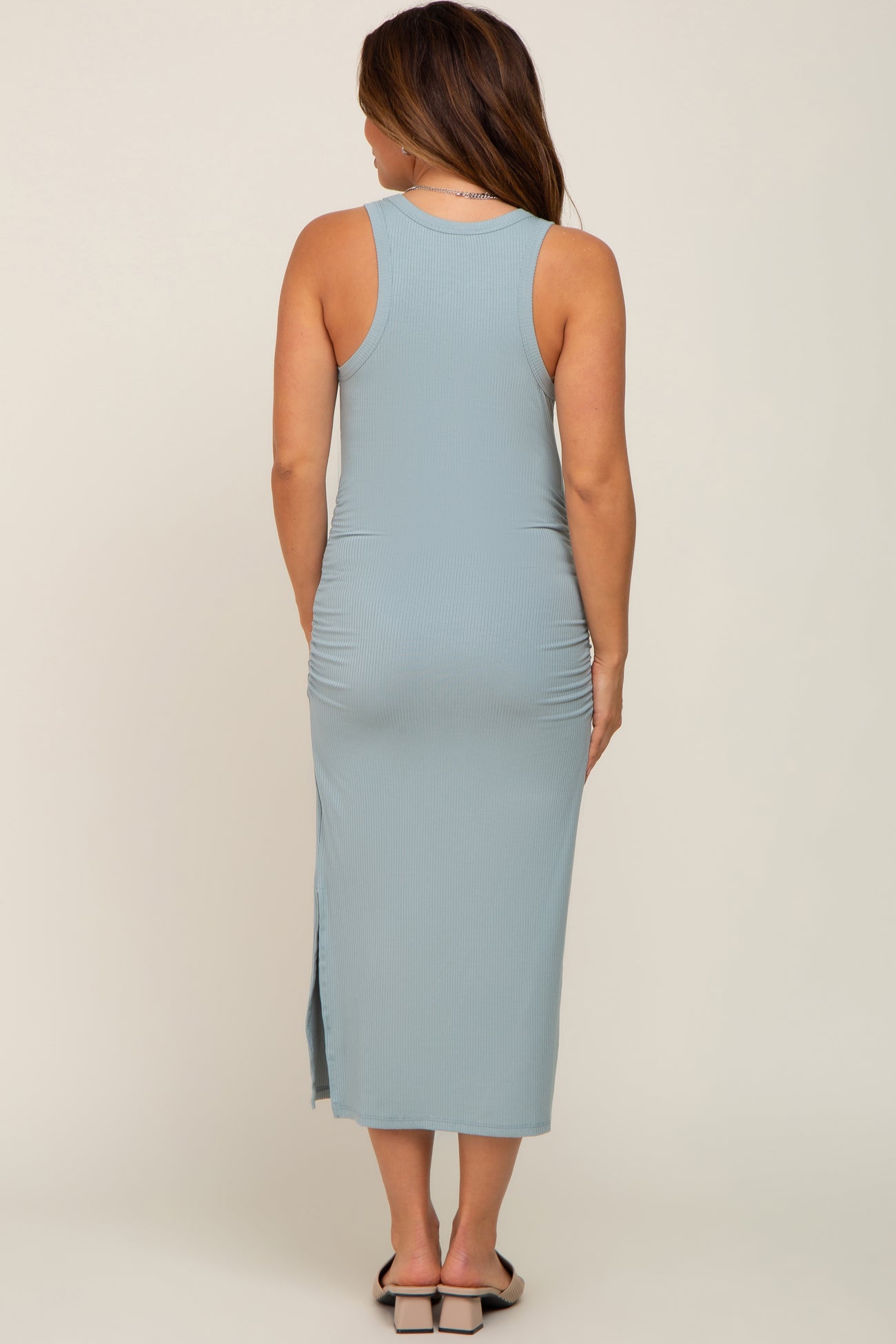 woman wearing a light blue sleeveless maternity midi dress with side slit, showing back view and a fitted silhouette