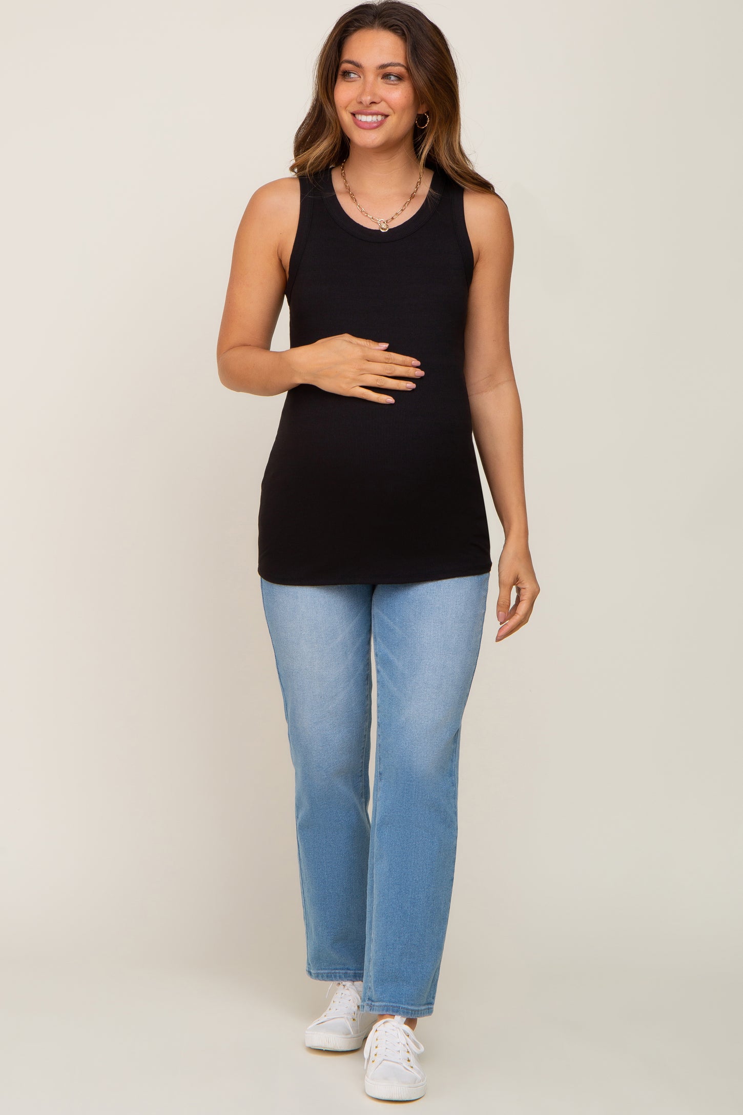 woman wearing a black tank top maternity wear and light blue jeans, holding her baby bump