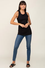 woman wearing a black sleeveless ribbed top and blue skinny jeans, posing with one hand on her hip