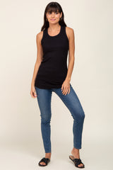 woman wearing a black sleeveless tank top and blue skinny jeans, standing with one hand on her hip