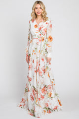 Woman wearing a long sleeve white floral maxi dress with orange and pink flowers and a waist tie