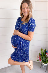 woman wearing a blue maternity dress with white leaf print, showing baby bump and smiling while holding her belly