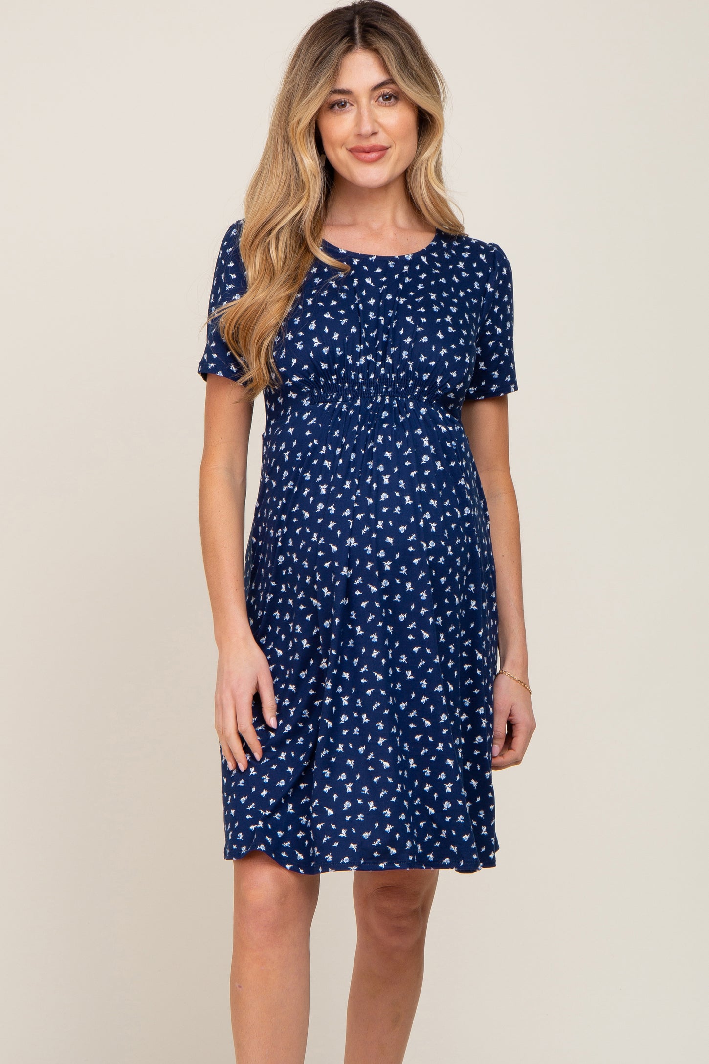 woman wearing a navy blue short sleeve maternity dress with white floral print and a gathered waist, showing a baby bump