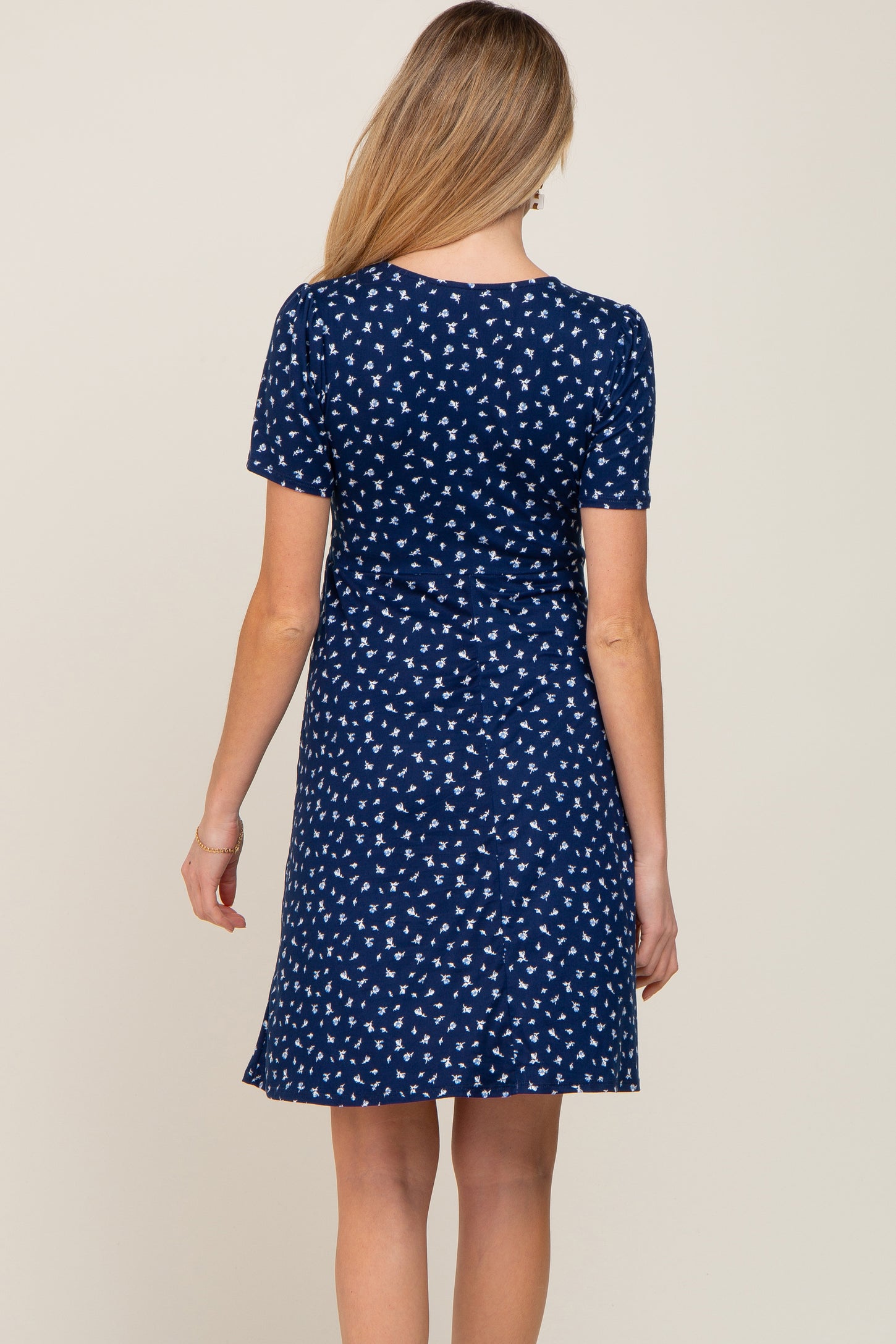 woman wearing a navy blue short sleeve maternity dress with a white floral print, showing the back view