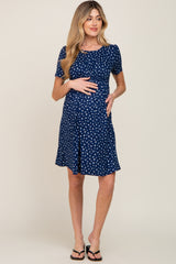 woman wearing a navy blue maternity dress with white polka dots and short sleeves, holding her baby bump