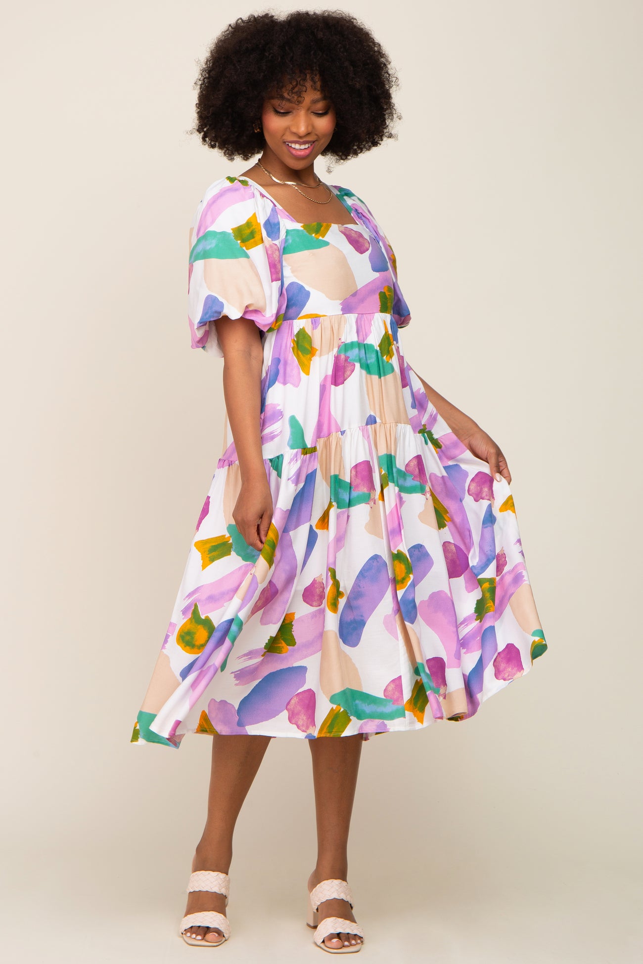 Woman wearing a colorful abstract print tiered midi dress with puff sleeves and a square neckline
