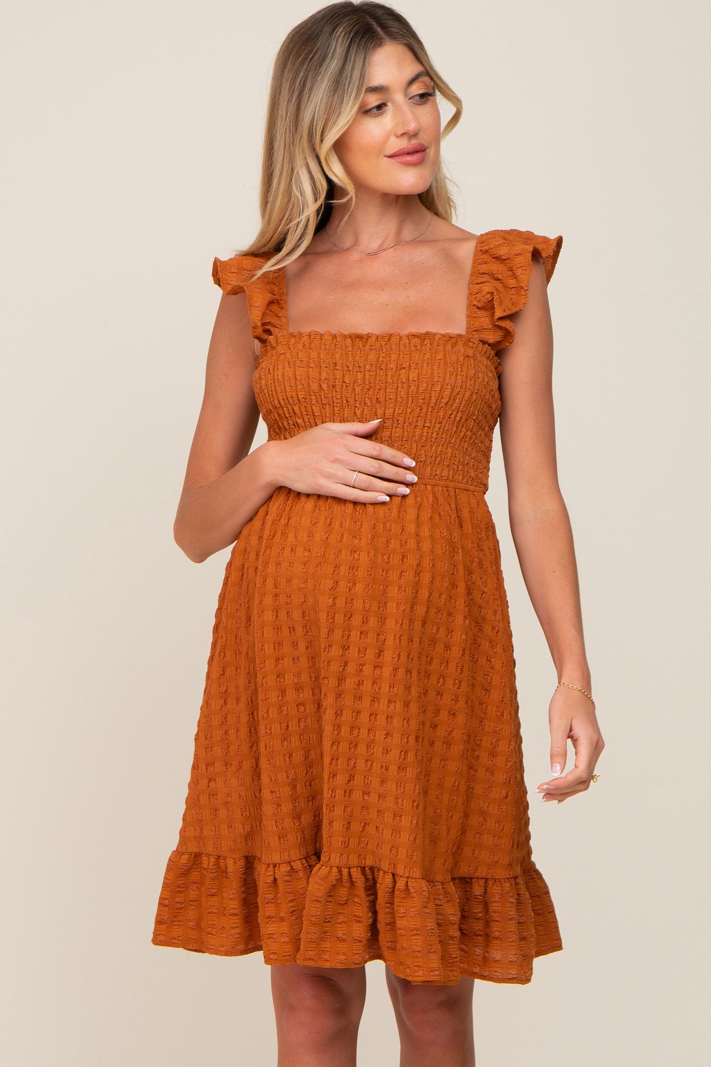 Pregnant woman wearing a rust orange smocked maternity dress with ruffle sleeves and a tiered hem